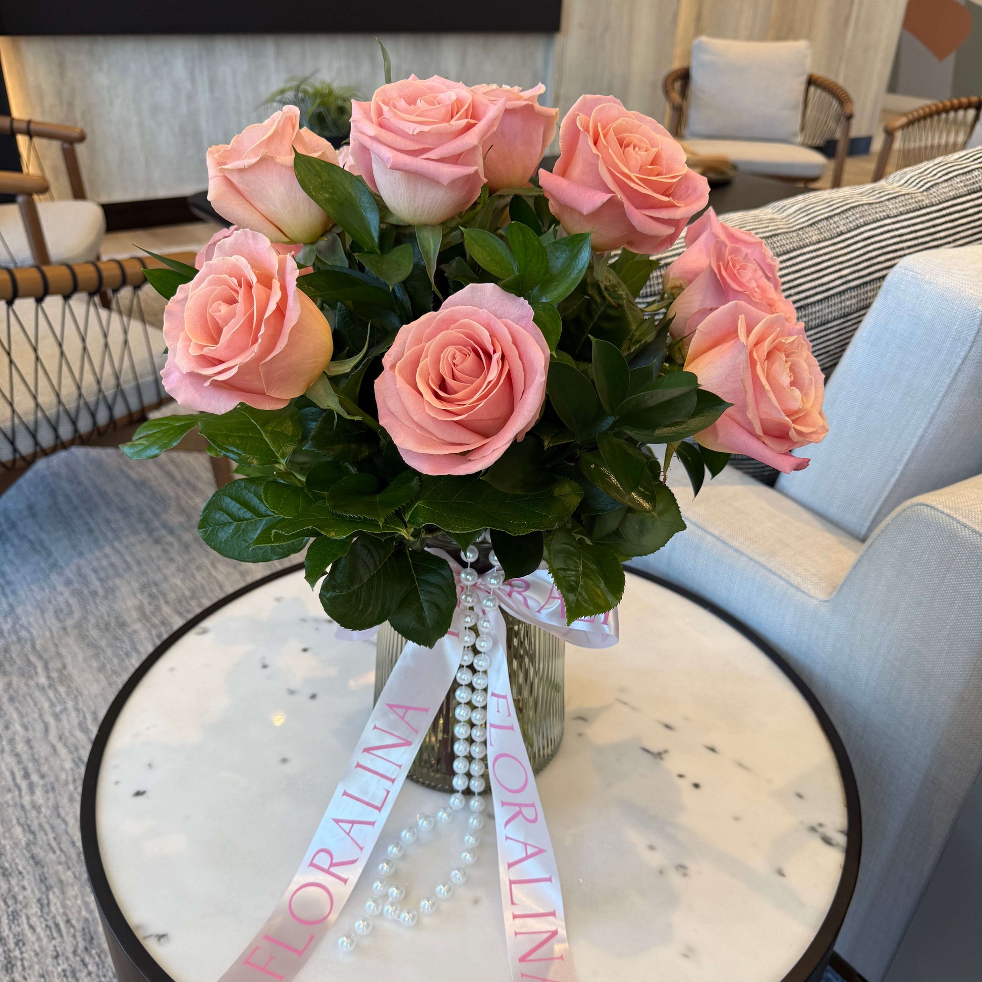 Bouquet of pink roses with a decorative ribbon on a round table in a living room setting.
